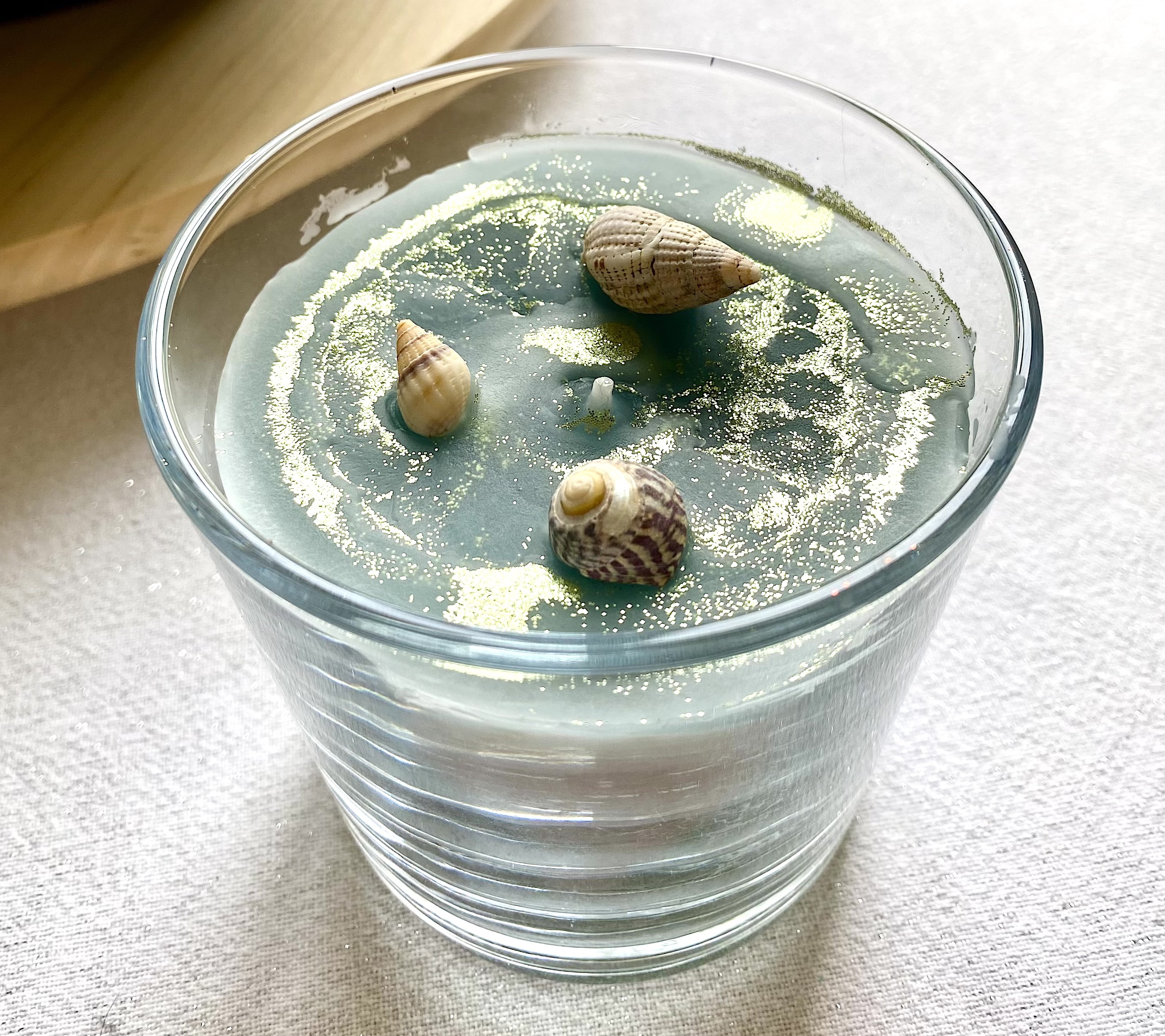 La nouvelle bougie est finalisée en ajoutant des coquillages récupérés sur la plage pendant les vacances.